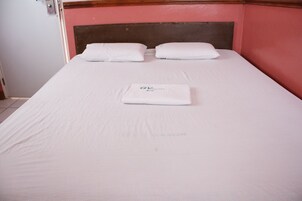 Una cama bien hecha con sábanas y almohadas blancas, una toalla doblada y un cartel con el número de la habitación y el nombre del hotel.