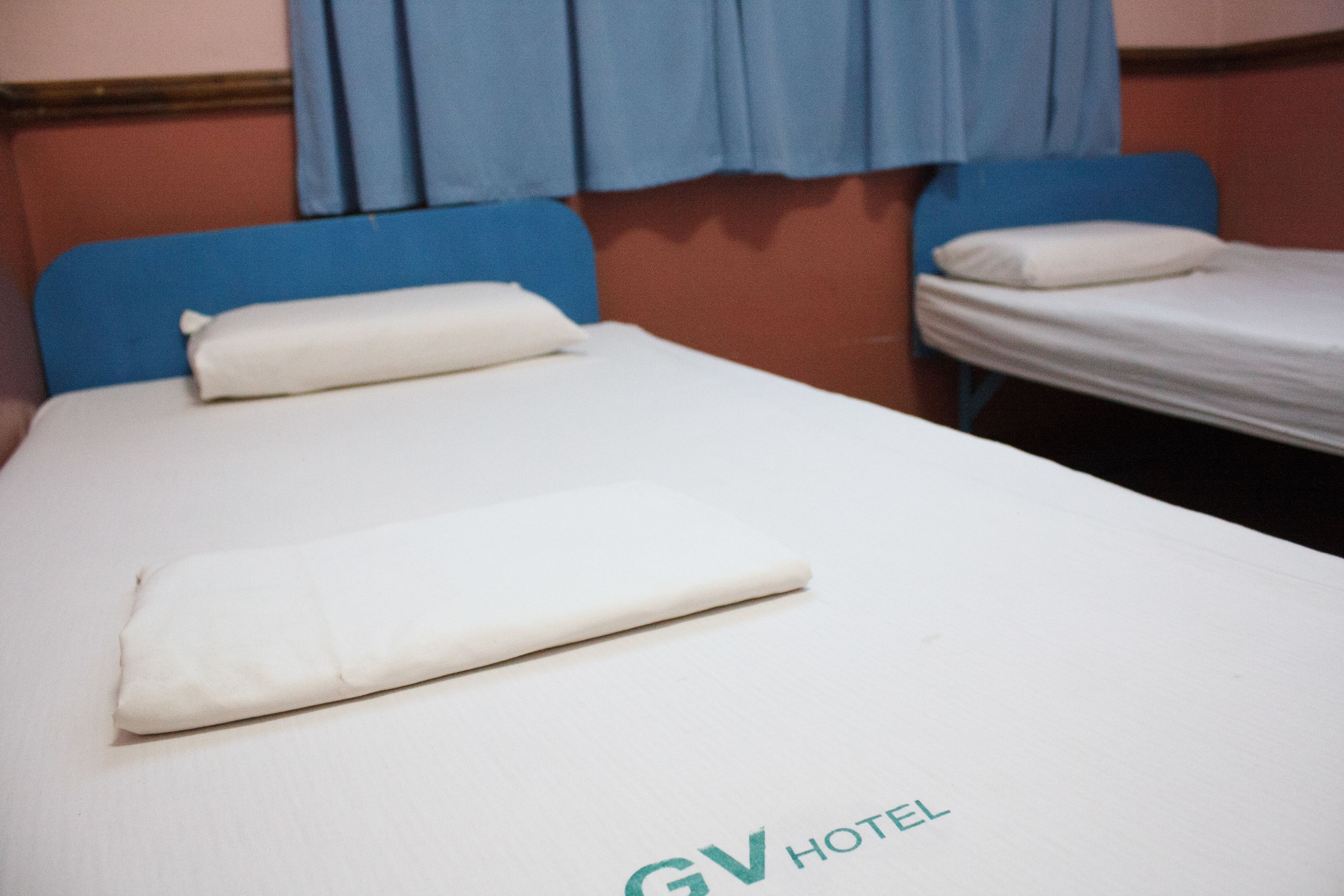 A single bed with a white mattress and blue headboard in a hotel room.