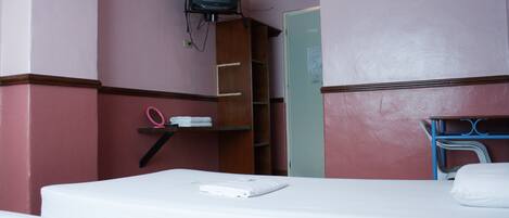 Una habitación de hotel con cama, televisión montada en la pared, armario y escritorio con silla.