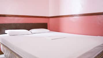 Una cama bien hecha con sábanas y almohadas blancas en una habitación con paredes rosadas y detalles de madera.