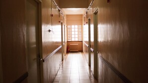 A corridor with doors on both sides, a tiled floor, and a window with a grid pattern at the end. - GV Hotel Maasin (Maasin City)