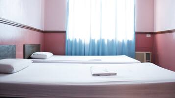 A hotel room with two beds, a window with blue curtains, and a radiator on the wall.