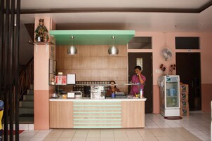Un área de recepción con mostrador, dos lámparas colgantes, una estatua en un estante, un refrigerador y una escalera.