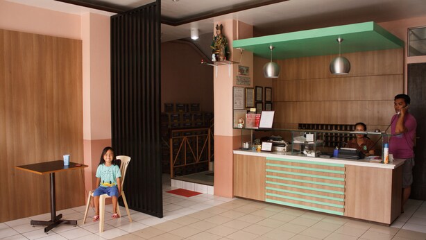A cafe with a wooden counter, a child seated at a table, and a person standing behind the counter. - GV Hotel Maasin (Maasin City)