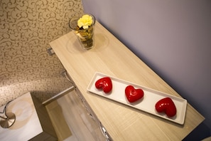 Una mesa de madera con un plato blanco que sostiene tres corazones rojos y un vaso con flores amarillas.