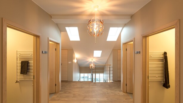 Un couloir doté d’un plancher en bois, d’un lustre central et de lucarnes.