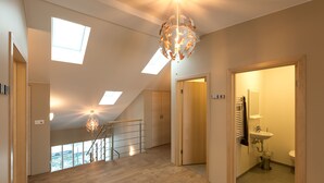 Un loft spacieux avec un escalier en bois, des fenêtres de toit et un lustre moderne.