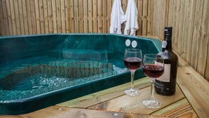 Une terrasse en bois avec un jacuzzi, deux verres de vin rouge et une bouteille de vin.