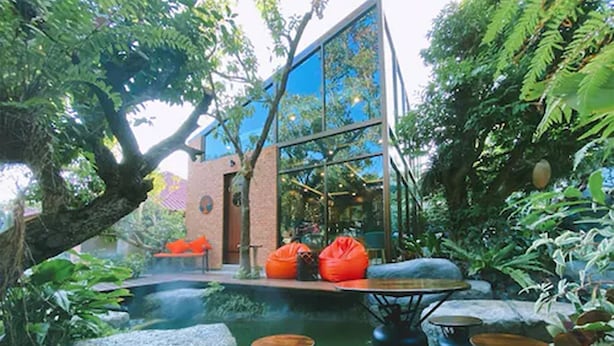 An outdoor seating area with a pond, surrounded by lush greenery and a modern building with large windows. - Floraville Phuket Resort (Chalong)