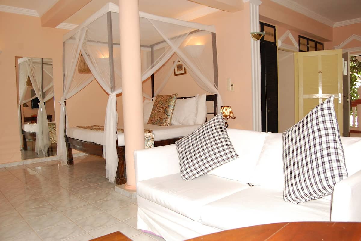 Una habitación con cama con dosel, un sofá blanco con almohadones cuadriculados y un espejo que refleja parte de la habitación.