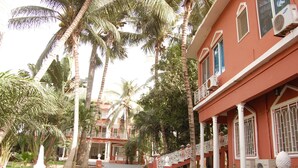 Un edificio rojo con columnas y balcones blancos, rodeado de palmeras.