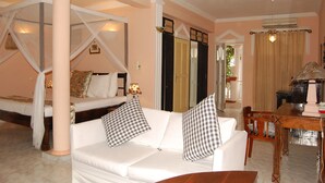 Un dormitorio con cama a dosel, un sofá blanco con almohadones a cuadros, una mesa de comedor de madera y un ventilador de techo.
