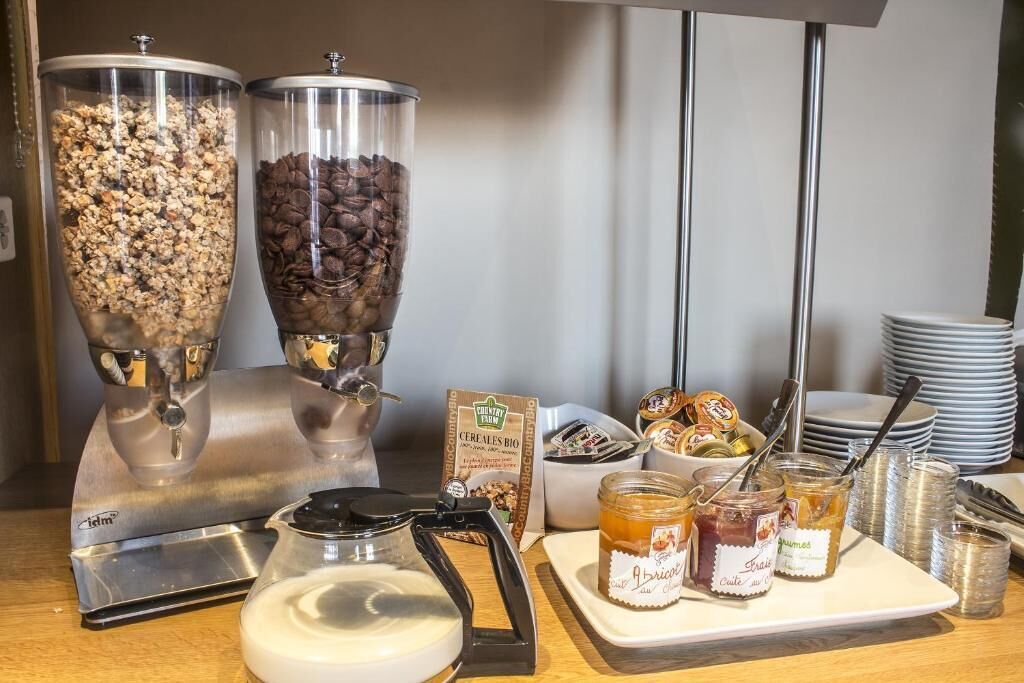 Una mesa de buffet con dos grandes dispensadores, una cafetera y una bandeja con frascos de mermelada.