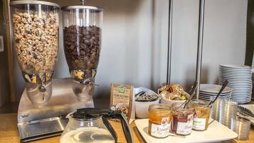 Una mesa de buffet con dos grandes dispensadores, una cafetera y una bandeja con frascos de mermelada.