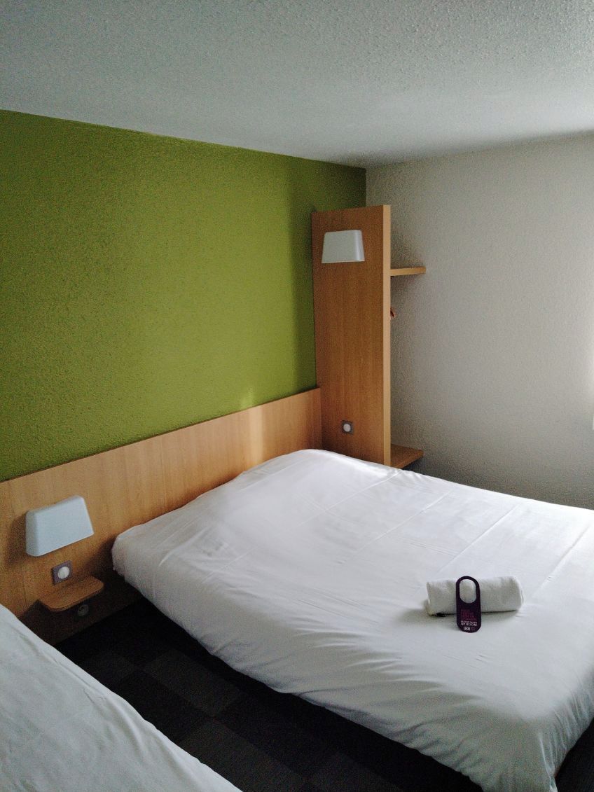 Een hotelkamer met een enkel bed, een houten hoofdeinde, een groene accentmuur en een nachtkastje met een lamp.