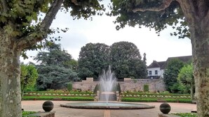 Un jardín formal con una fuente central, rodeado de setos cuidadosamente recortados y diversas especies de árboles.
