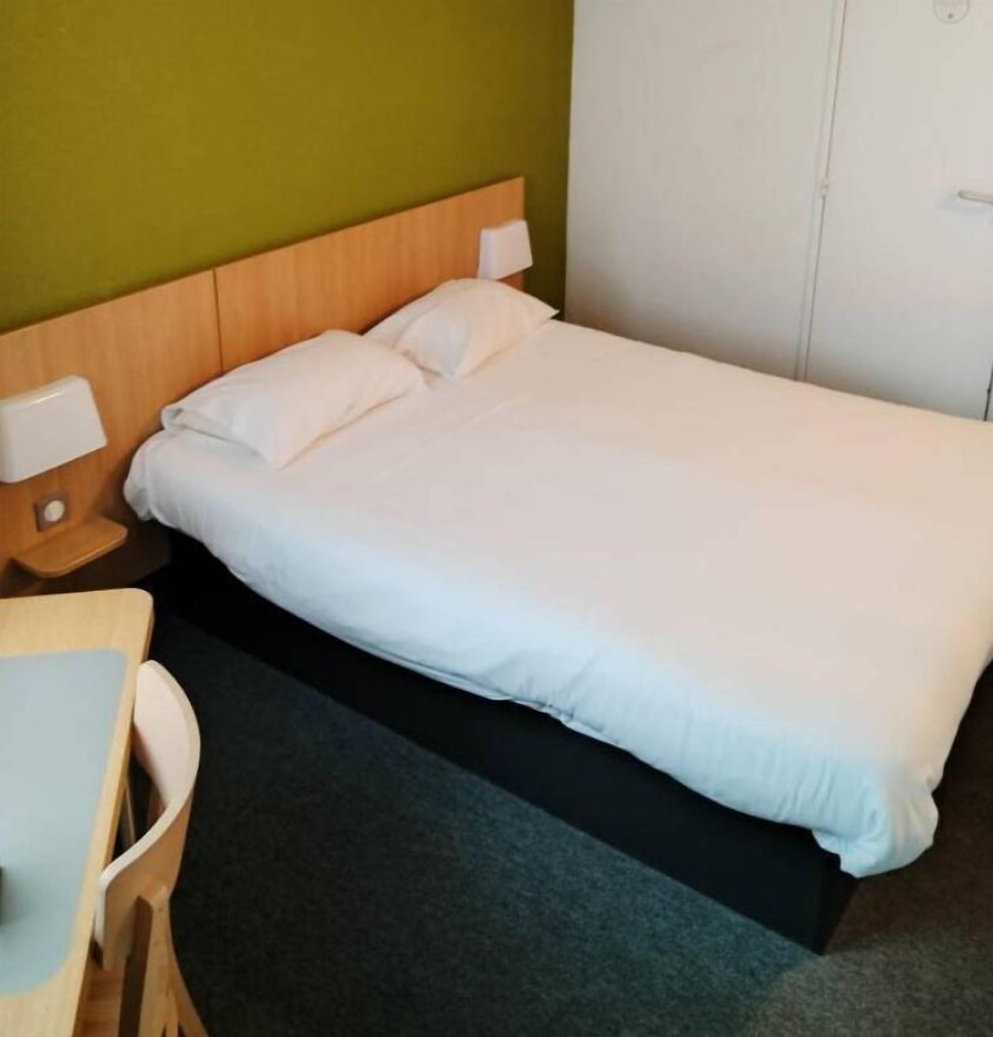 Un lit simple avec une literie blanche, dans une pièce dont un mur est vert et la porte est blanche.