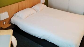 A single bed with white bedding in a room with a green wall and a white door.