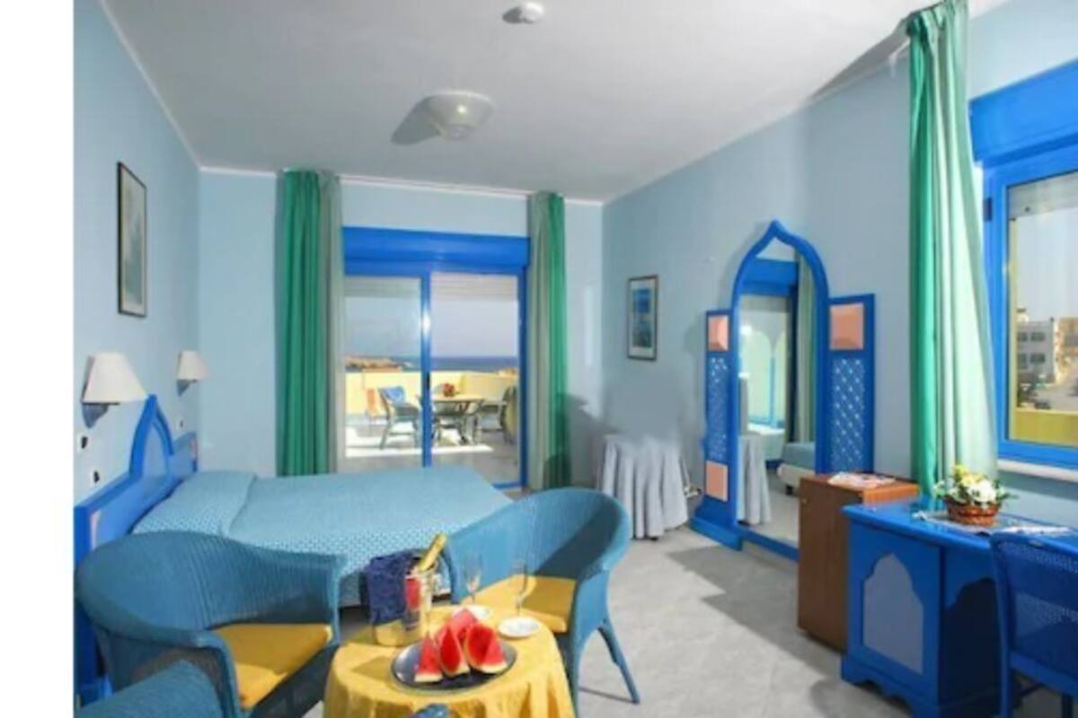A room with a bed, a small table with a yellow tablecloth, and a window with blue curtains.