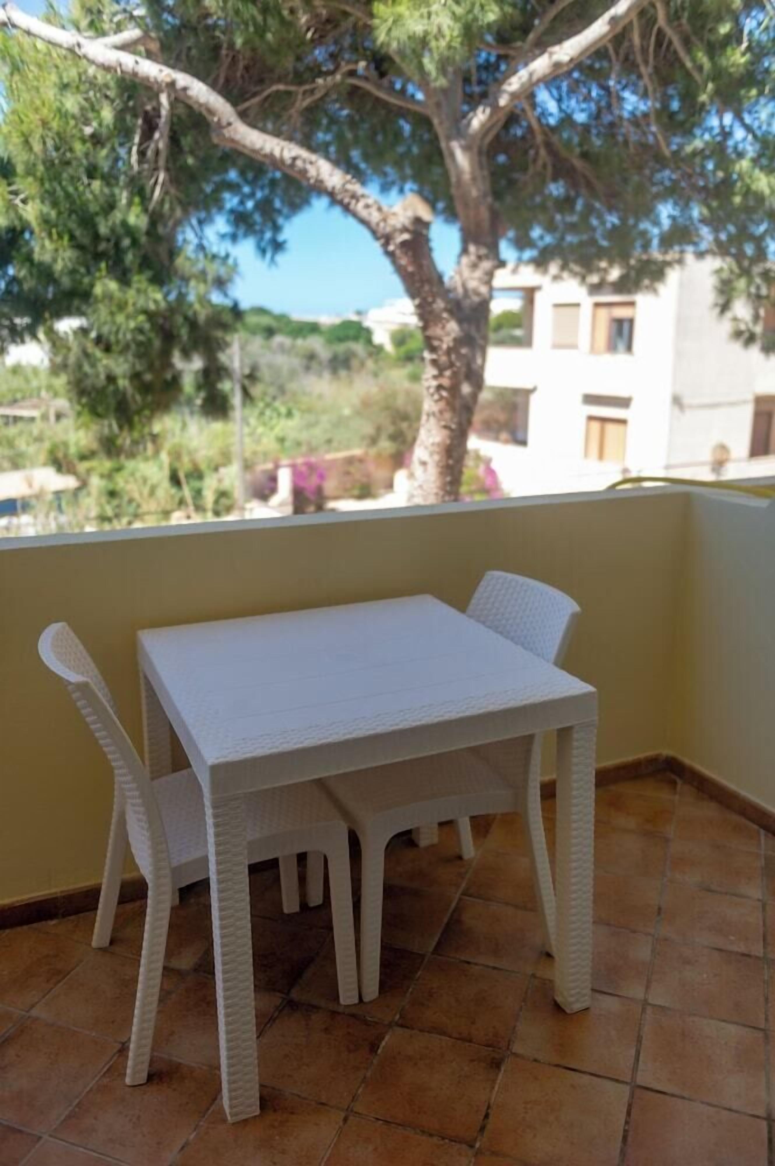 A white plastic table and chairs on a balcony with a tiled floor, overlooking a building and trees.