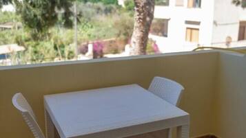 A white plastic table and chairs on a balcony with a tiled floor, overlooking a building and trees.