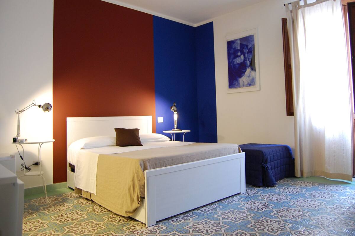 A bedroom with a bed, bedside table, lamp, and a window with curtains.