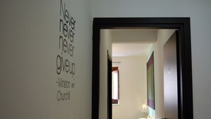 A room with a bed, a wall with a quote, and a door leading to another room.