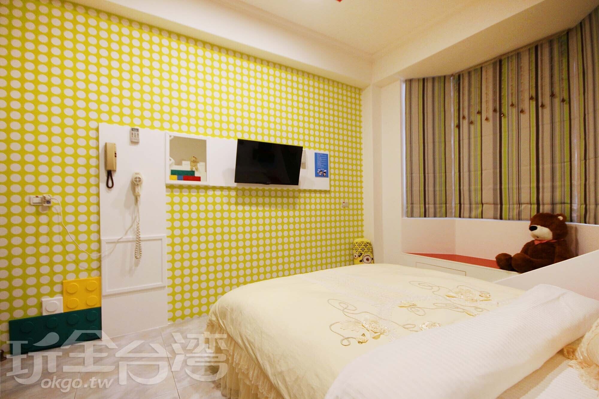 A bedroom with a bed, a TV mounted on the wall, a telephone, and a window with curtains.