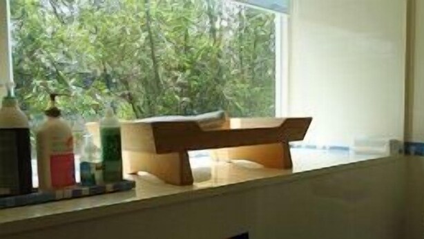 Une salle de bain avec un banc en bois, une fenêtre donnant sur un paysage verdoyant et des articles de toilette posés sur le comptoir.