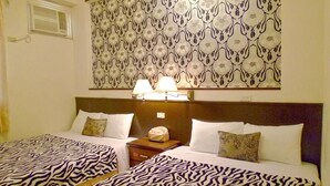 Une chambre d’hôtel avec deux lits, des rideaux à motifs, une table de chevet avec des lampes et un climatiseur fixé au mur.