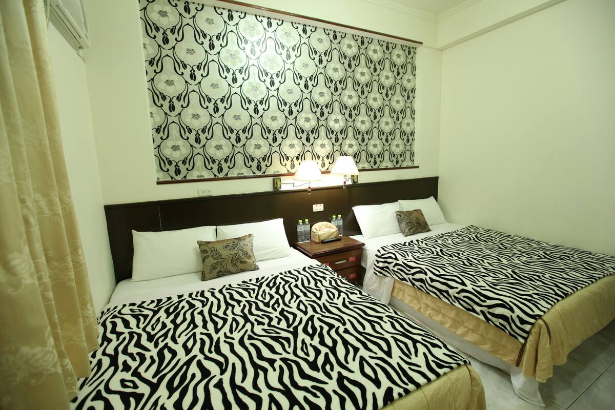 Habitación de hotel con dos camas, cabecero estampado, lámparas de noche y un adorno en la pared.