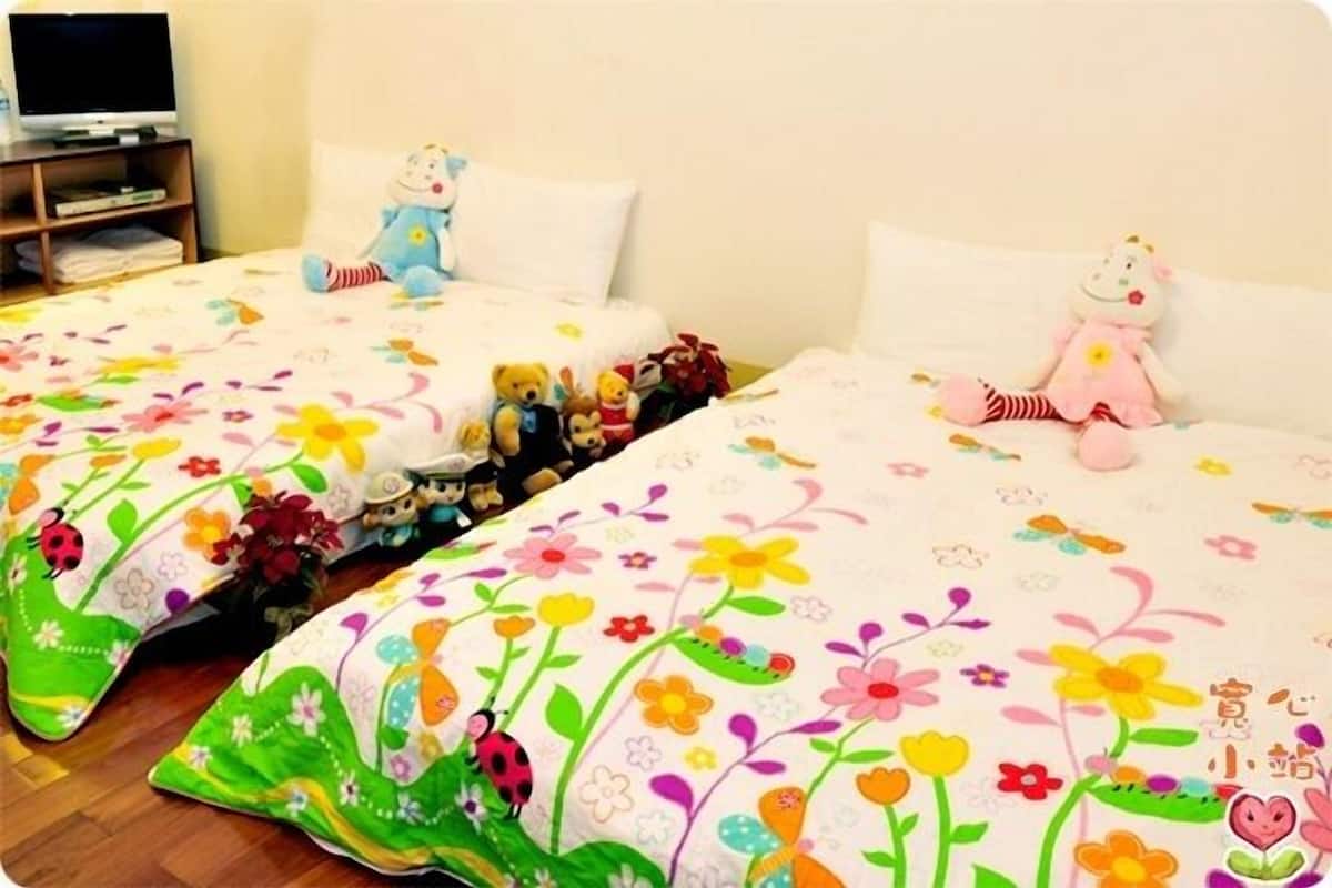 Habitación de hotel con dos camas, cada una con una colcha estampada con motivos florales y peluches.