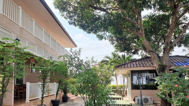 A courtyard with outdoor seating, a staircase leading to a building entrance, and a large tree providing shade. - Sea Beach Koh Larn (Koh Lan)
