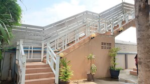A staircase with white railings leading to a covered area, surrounded by potted plants and a tree. - Sea Beach Koh Larn (Koh Lan)