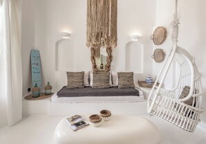 A modern, minimalist room with a white sofa, a hanging macrame piece, a white wicker chair, and decorative baskets. - Captain Zeppos (Milos)