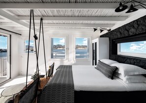 Un dormitorio moderno con una cama grande, dos ventanas con vistas al océano, una silla colgante y un techo con un diseño único.