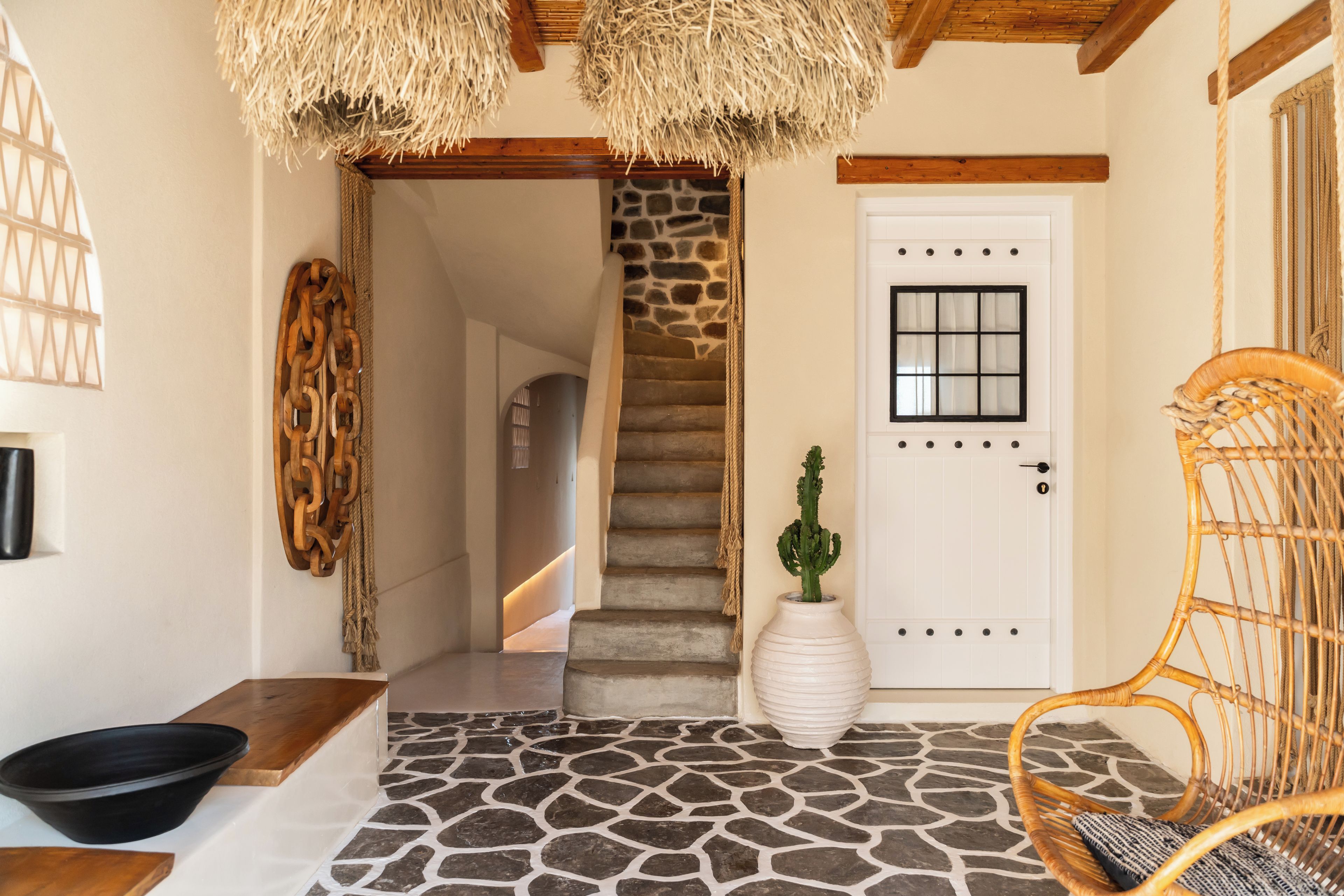 A stone-tiled entrance with a white door, a wicker chair, and a cactus plant.