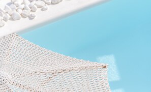 A white crocheted beach chair with a clear view of the sky and a pool. - Captain Zeppos (Milos)