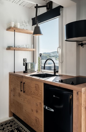 A modern kitchen with wooden cabinetry, a black dishwasher, and a window overlooking a scenic view. - Captain Zeppos (Milos)