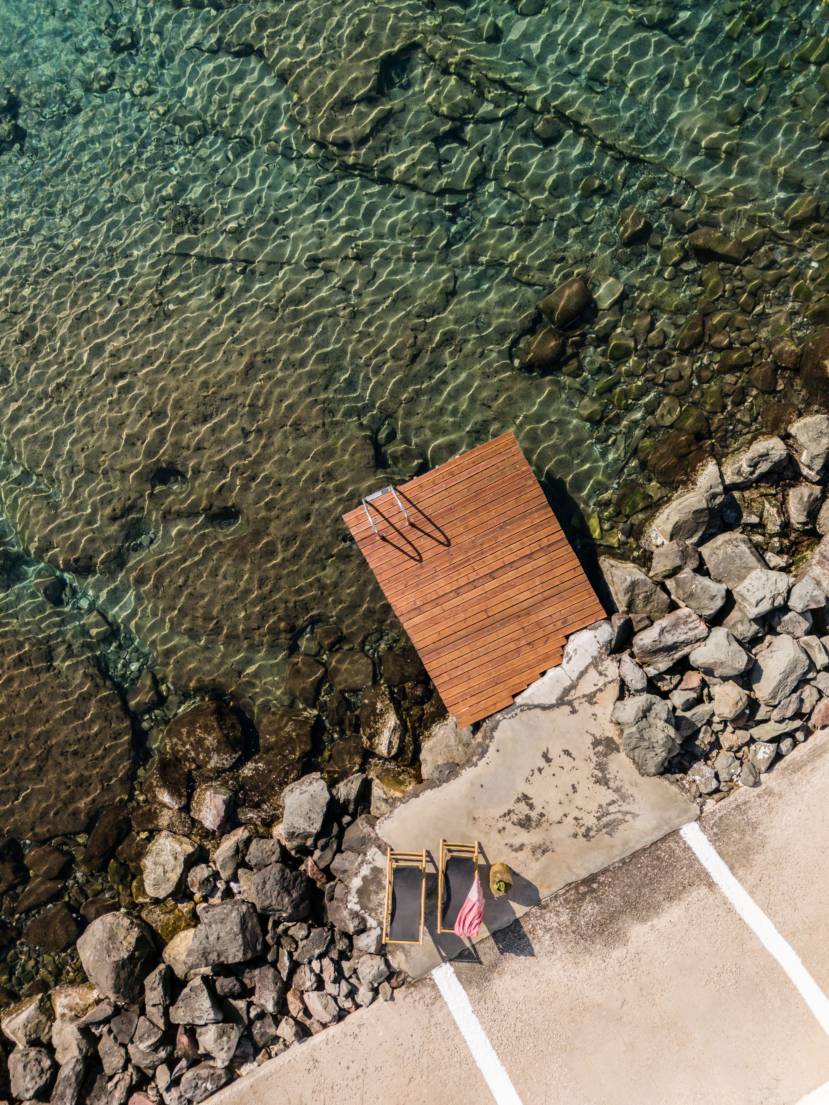 A wooden deck with a railing, a concrete pathway, and a rocky shoreline.