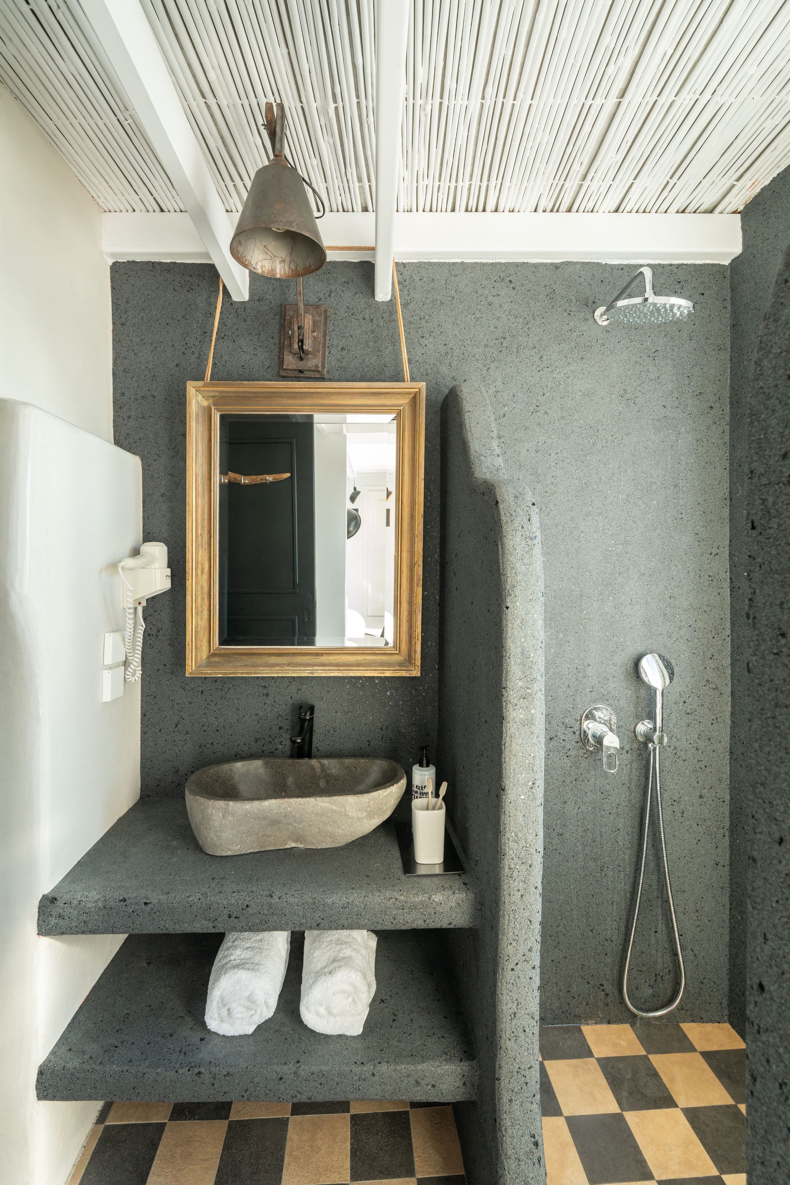 Un baño con lavamanos de piedra, espejo con marco de madera, ducha y piso a cuadros.