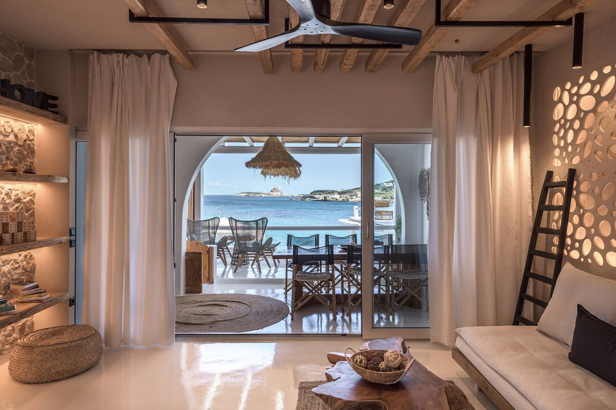 Ein modernes Wohnzimmer mit Meerblick, ausgestattet mit einer Couch, einem Essbereich und einer Steinwand mit der Aufschrift 'HOME'.