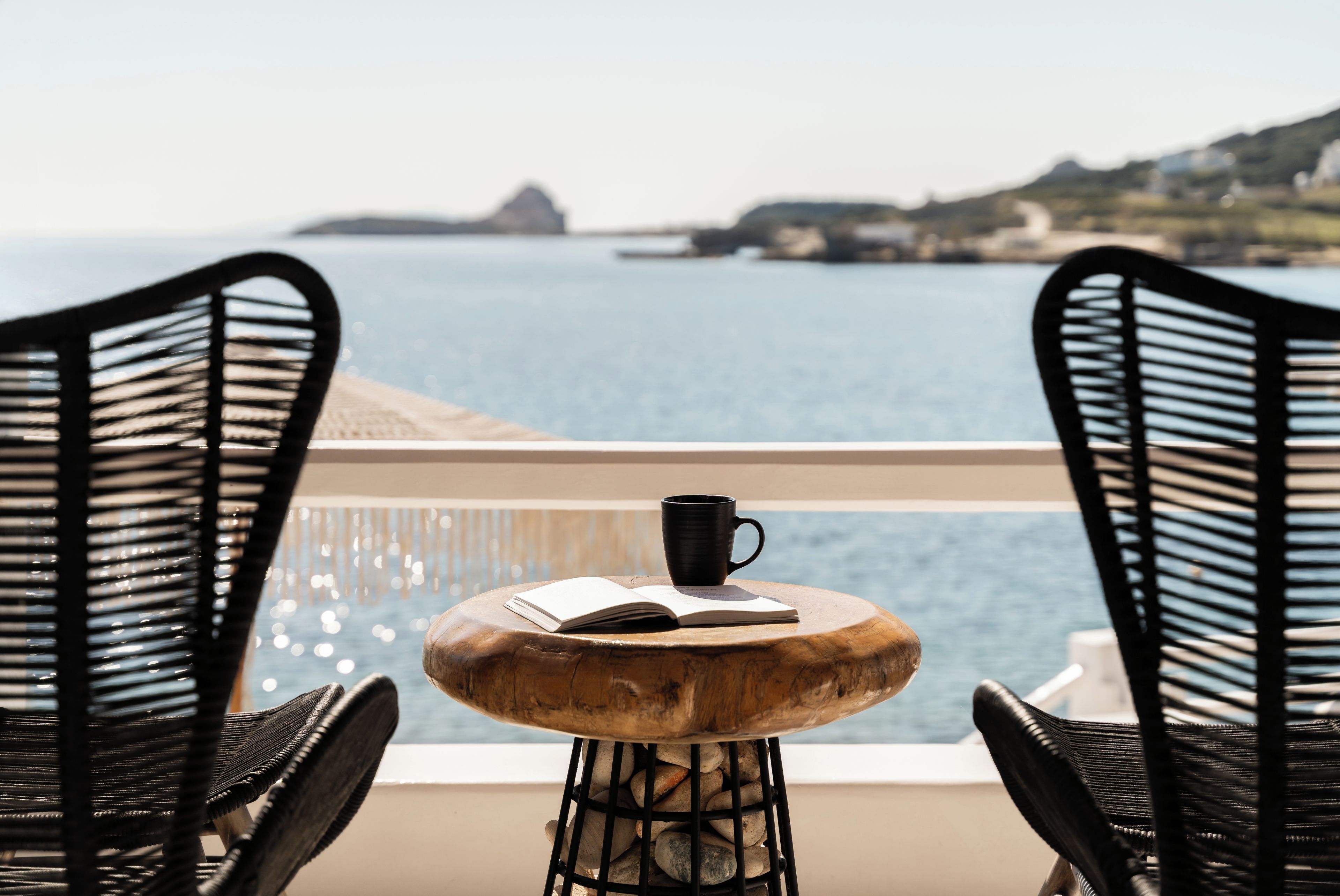 Een balkon met twee rieten stoelen, een kleine ronde tafel en een zwarte mok.