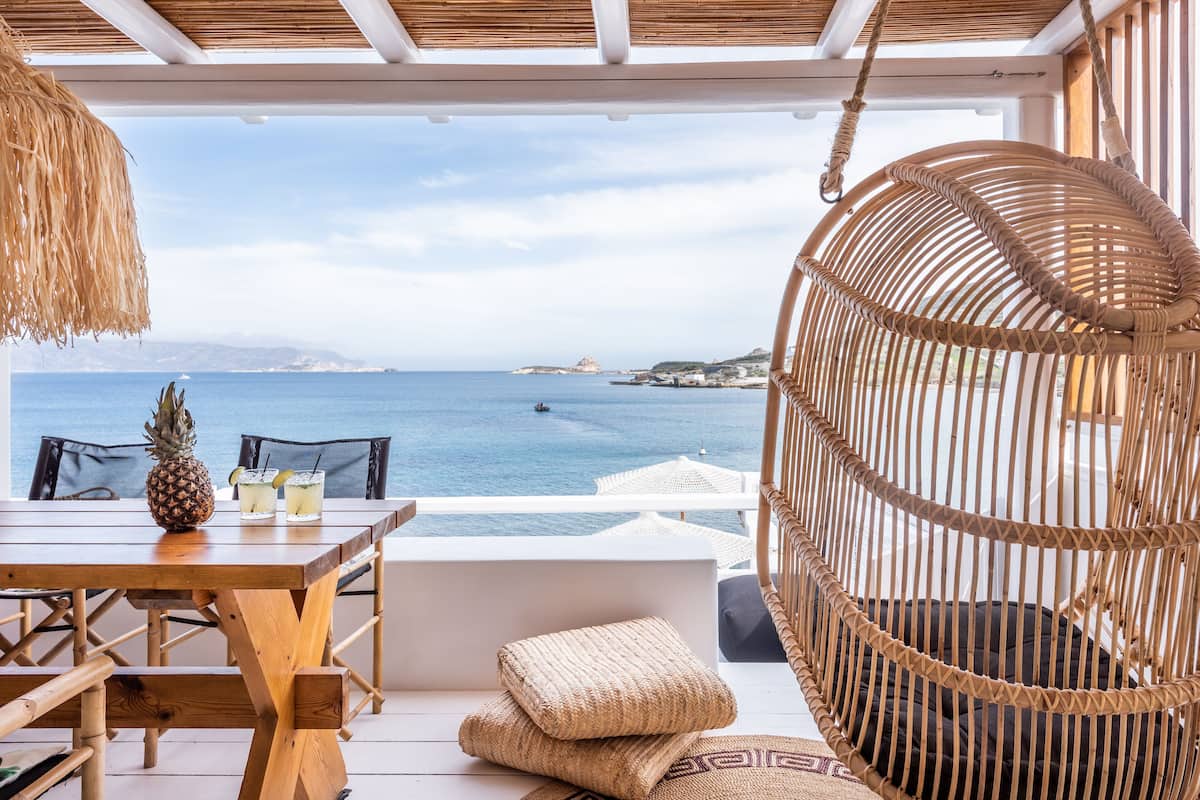 Ein Holztisch mit einer Ananas und zwei Getränken, ein Korbstuhl und Blick auf das Meer.