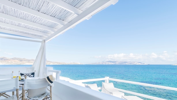 A white outdoor seating area with a view of the sea, a table with a hat, and a wicker lantern. - Captain Zeppos (Milos)