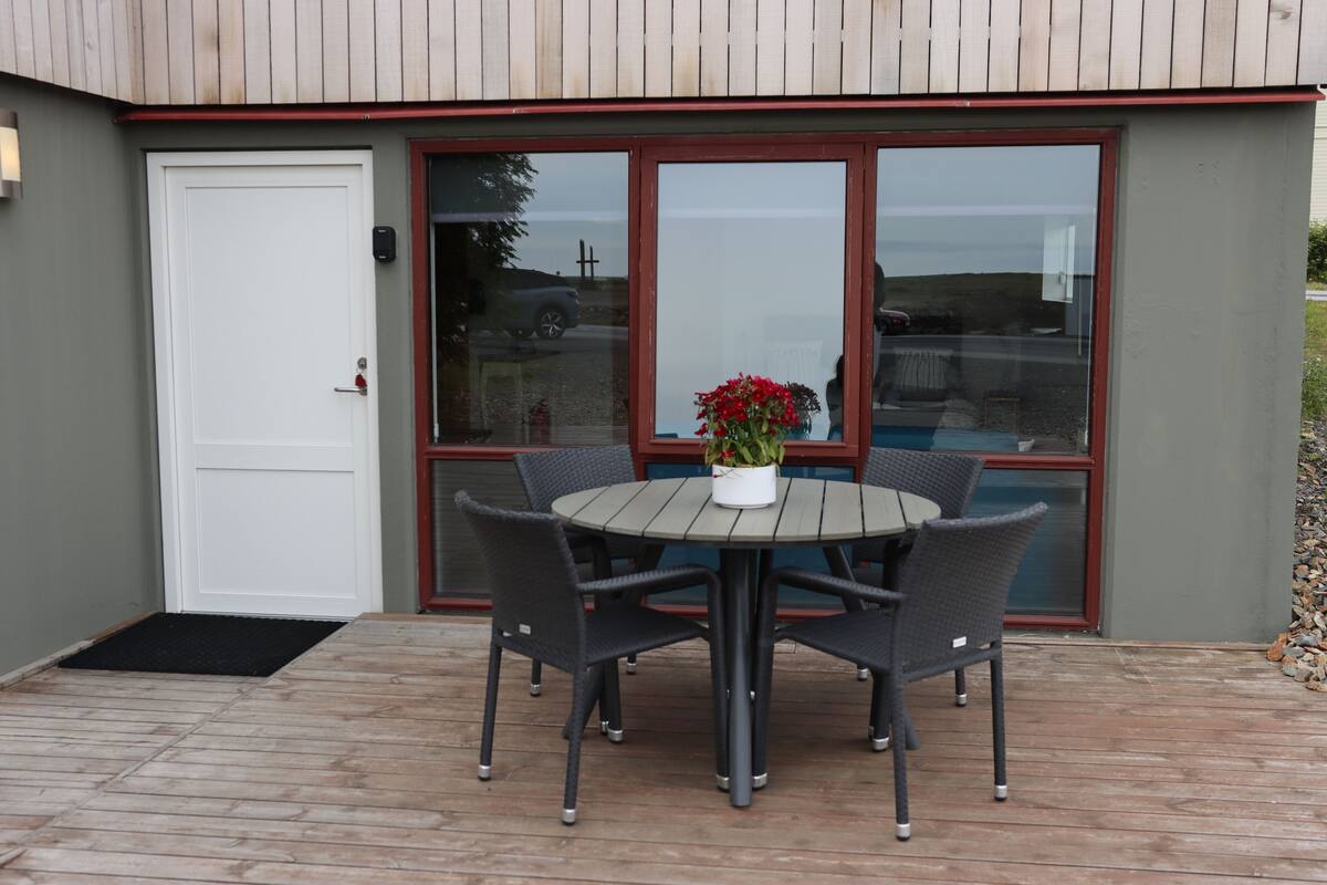 A patio with a round table and chairs, a white door, and a window with a red frame.