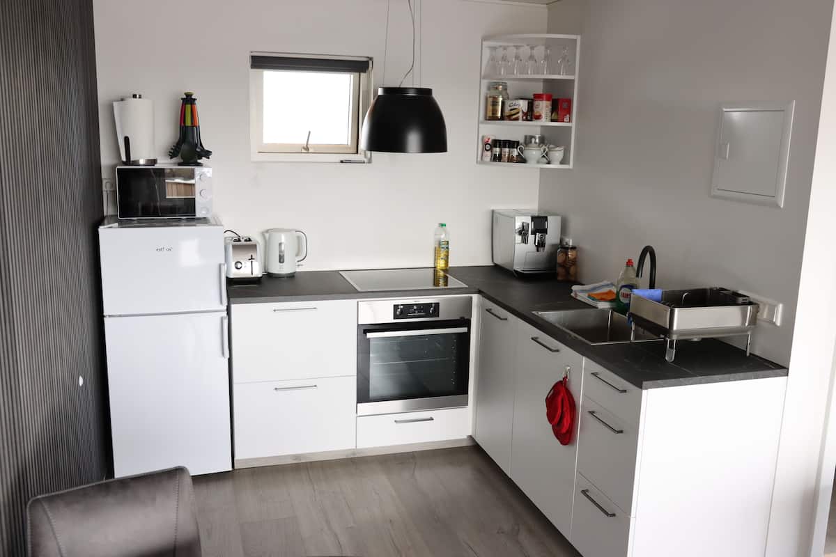 A modern kitchen with white cabinets, a built-in oven, a coffee maker, and a sink.