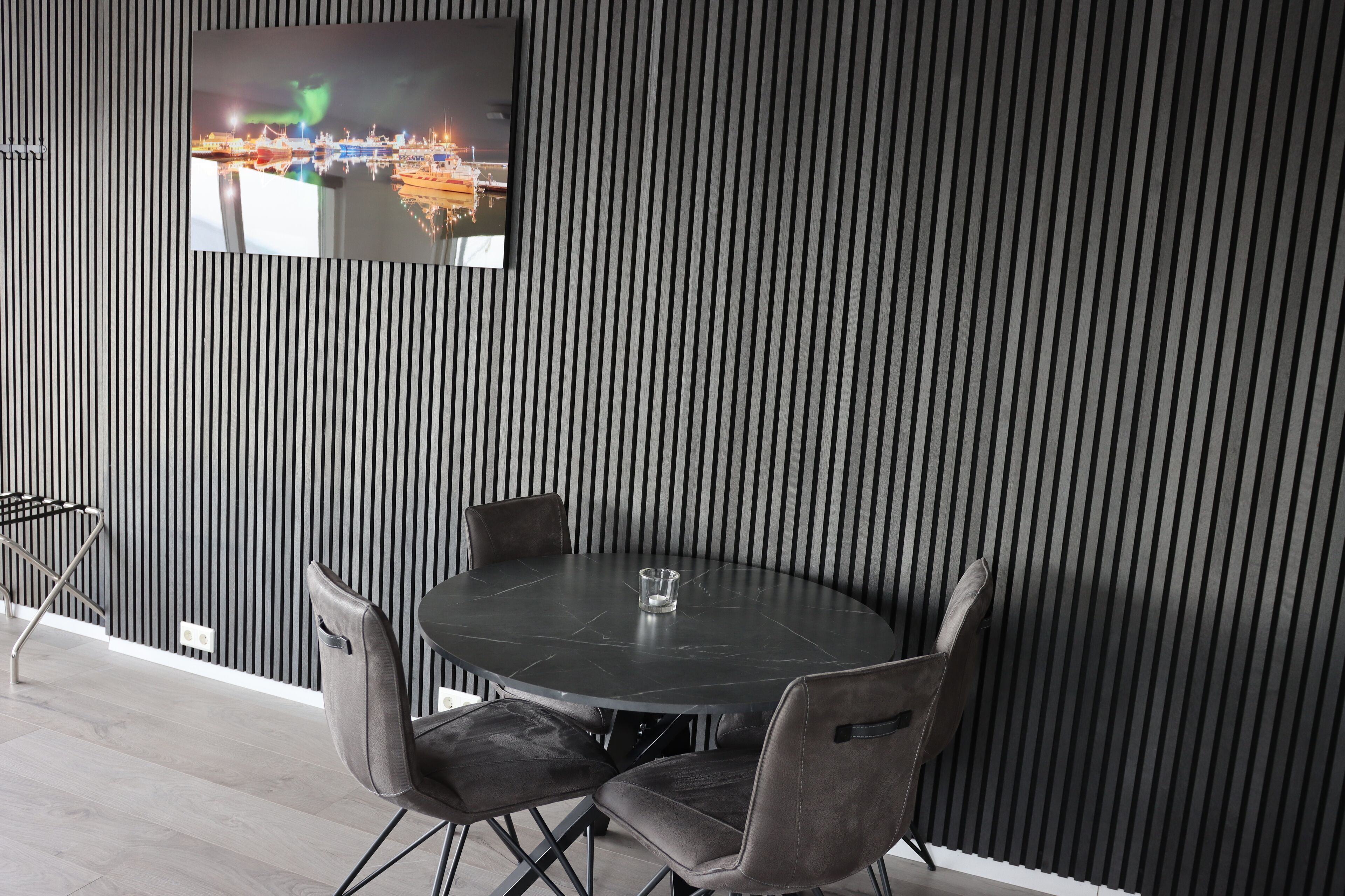 Un comedor moderno con una mesa redonda y cuatro sillas, un televisor en una pared a rayas, y un estante metálico a la izquierda.