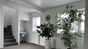 Een ruime hal met vloerbedekking, een trap, een witte radiator en twee potplanten.