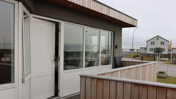 Een modern gebouw met grote glasramen, een houten terras en een deur.